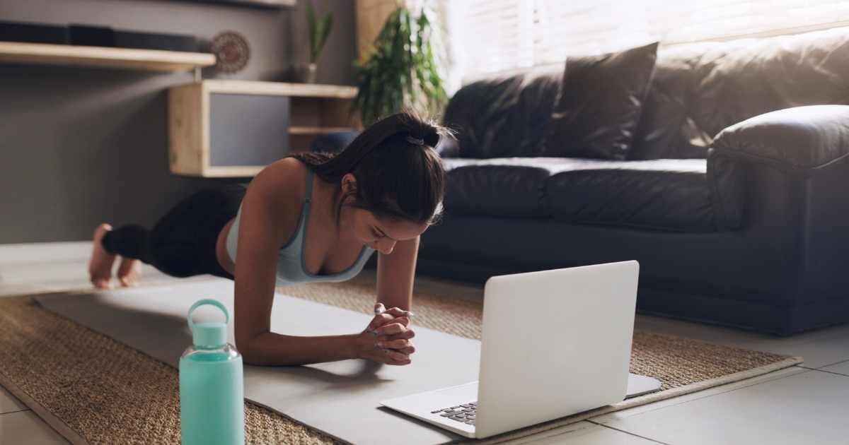  A woman doing a plank exercise while watching a workout on her laptop in her living room.